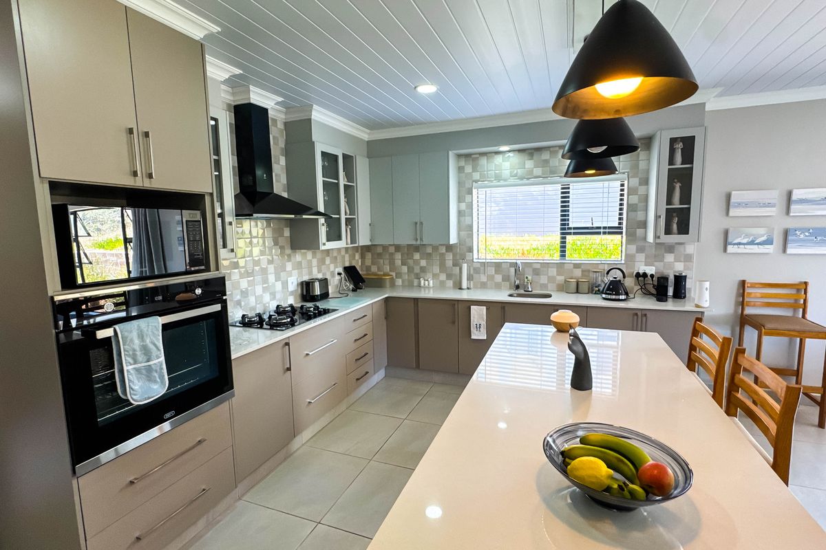 Modern kitchen featuring a central island, built-in oven, gas hob, extractor fan, tiled backsplash, and ample cabinetry with a clean, contemporary finish.