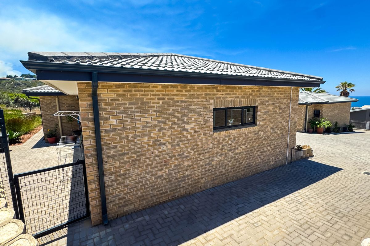 Exterior view of the property featuring face brick walls, tiled roof, and paved driveway area with ocean views in the background.