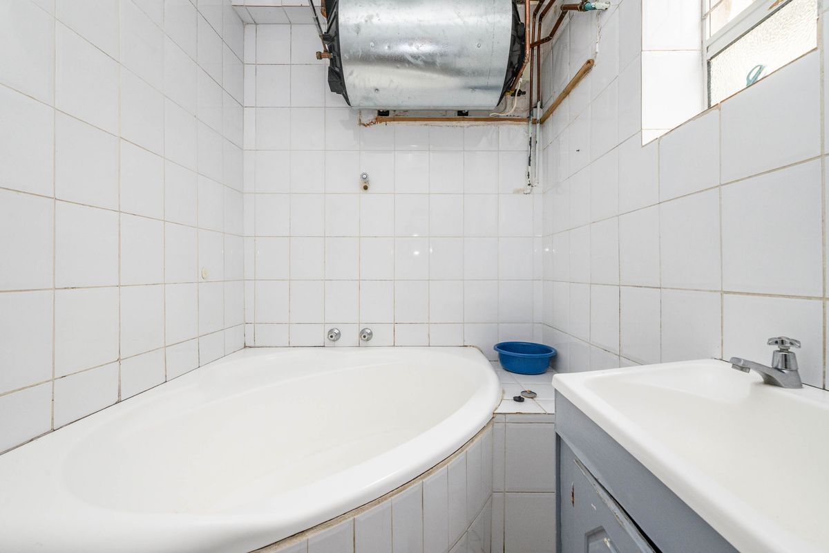 A compact bathroom featuring a built-in bathtub and vanity basin, with exposed water heating infrastructure and tiled wall finishes.
