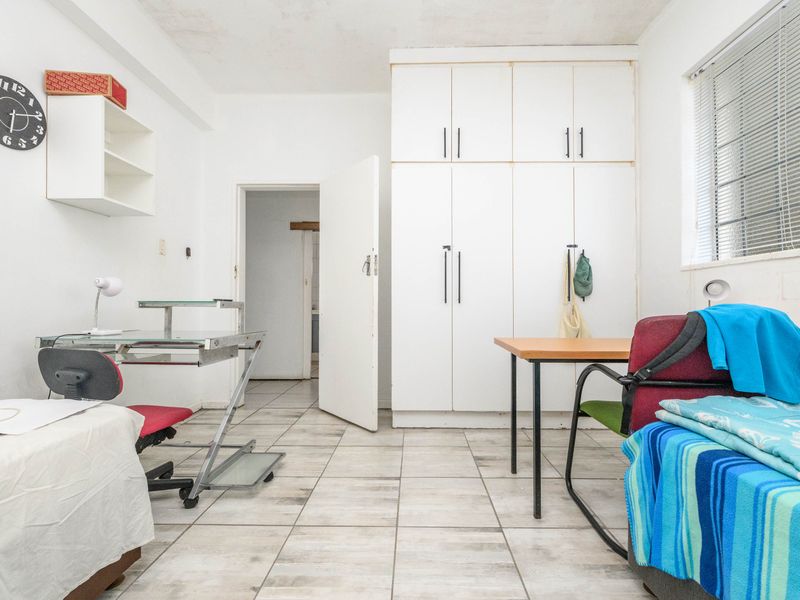 A functional bedroom featuring tiled flooring, built-in storage cupboards, and natural light through a window with venetian blinds.