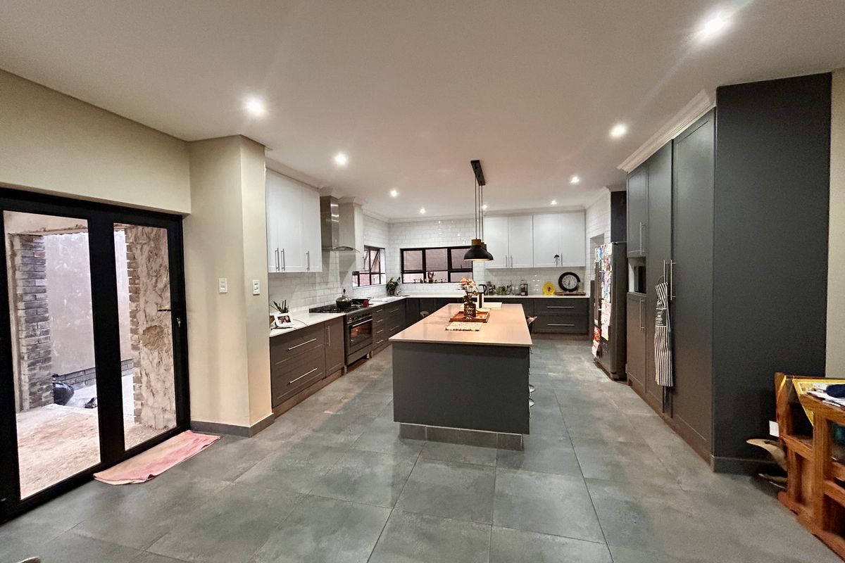 Modern open-plan kitchen featuring a large central island, dark cabinetry, subway tile backsplash, and direct access to an outdoor area through sliding glass doors.
