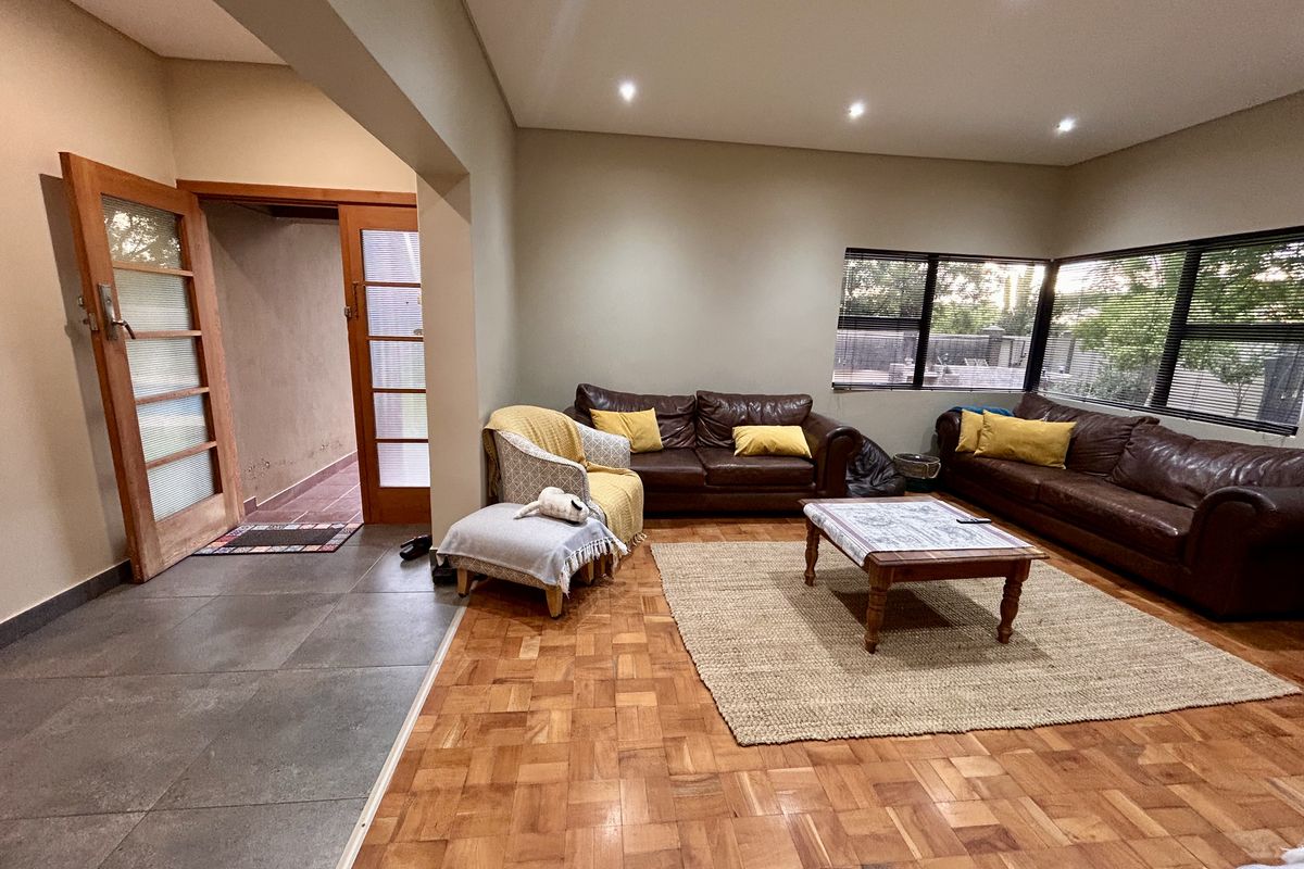 Spacious living room featuring warm parquet flooring, recessed downlighting, and large corner windows that provide ample natural light and garden views.