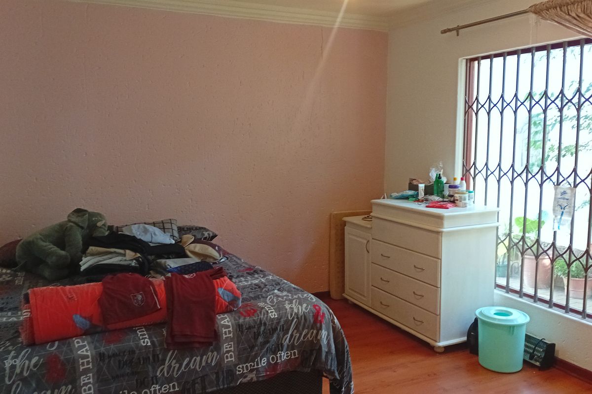 A bedroom featuring laminate flooring, textured pink walls, and a window fitted with a metal security gate.