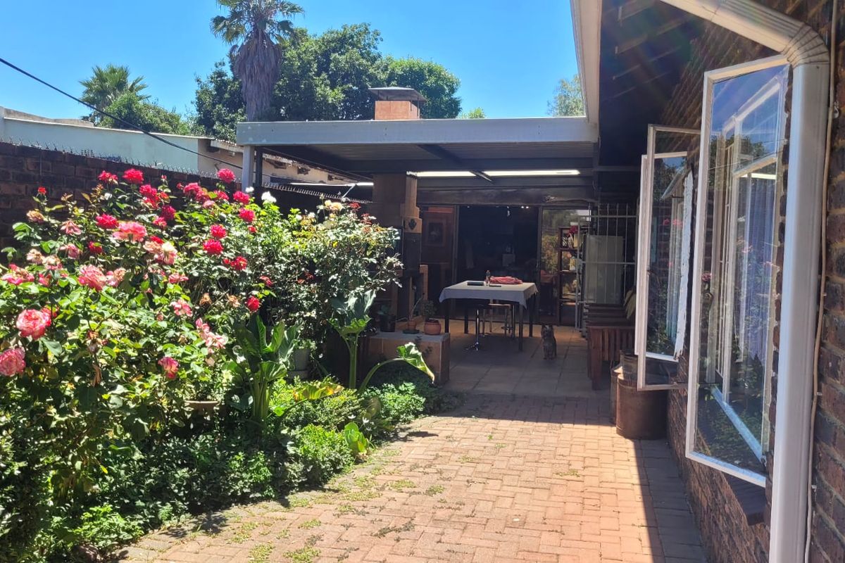 A private rear courtyard featuring a covered patio area, brick paving, and established garden beds with rose bushes.