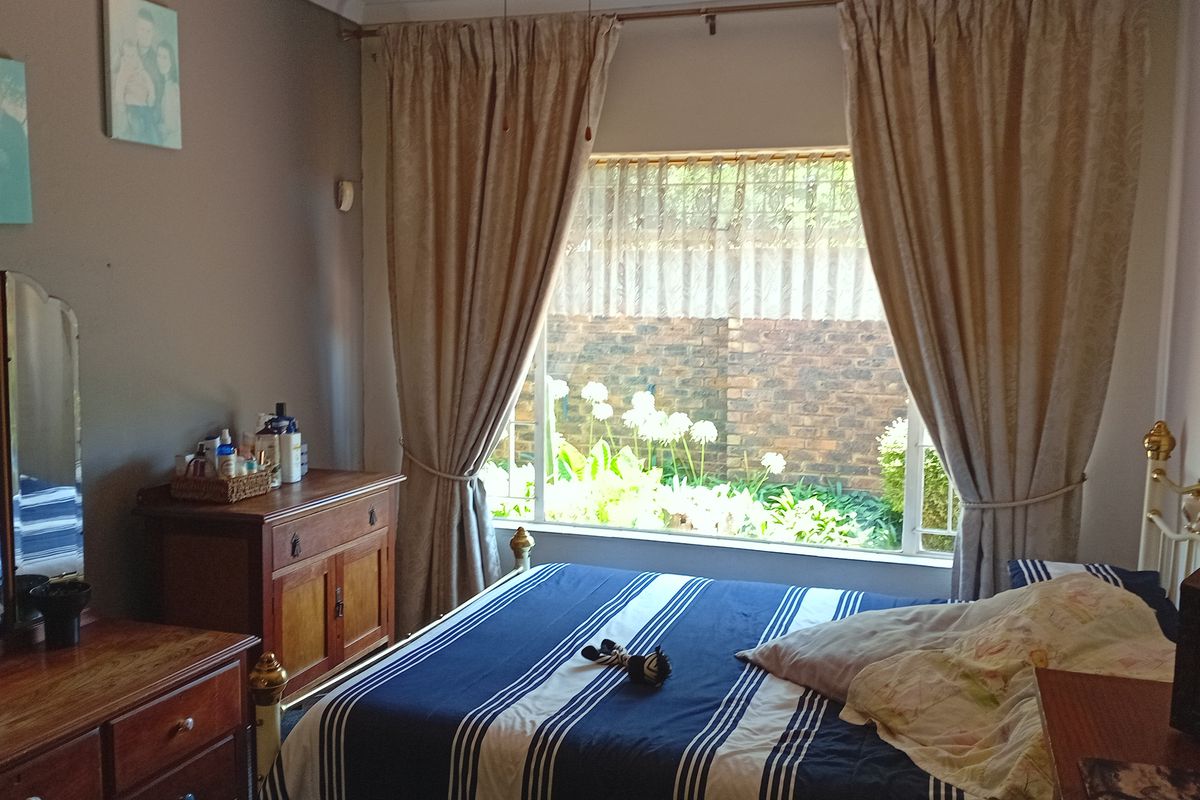 A bedroom featuring a large window with garden views, neutral wall tones, and classic curtain treatments.