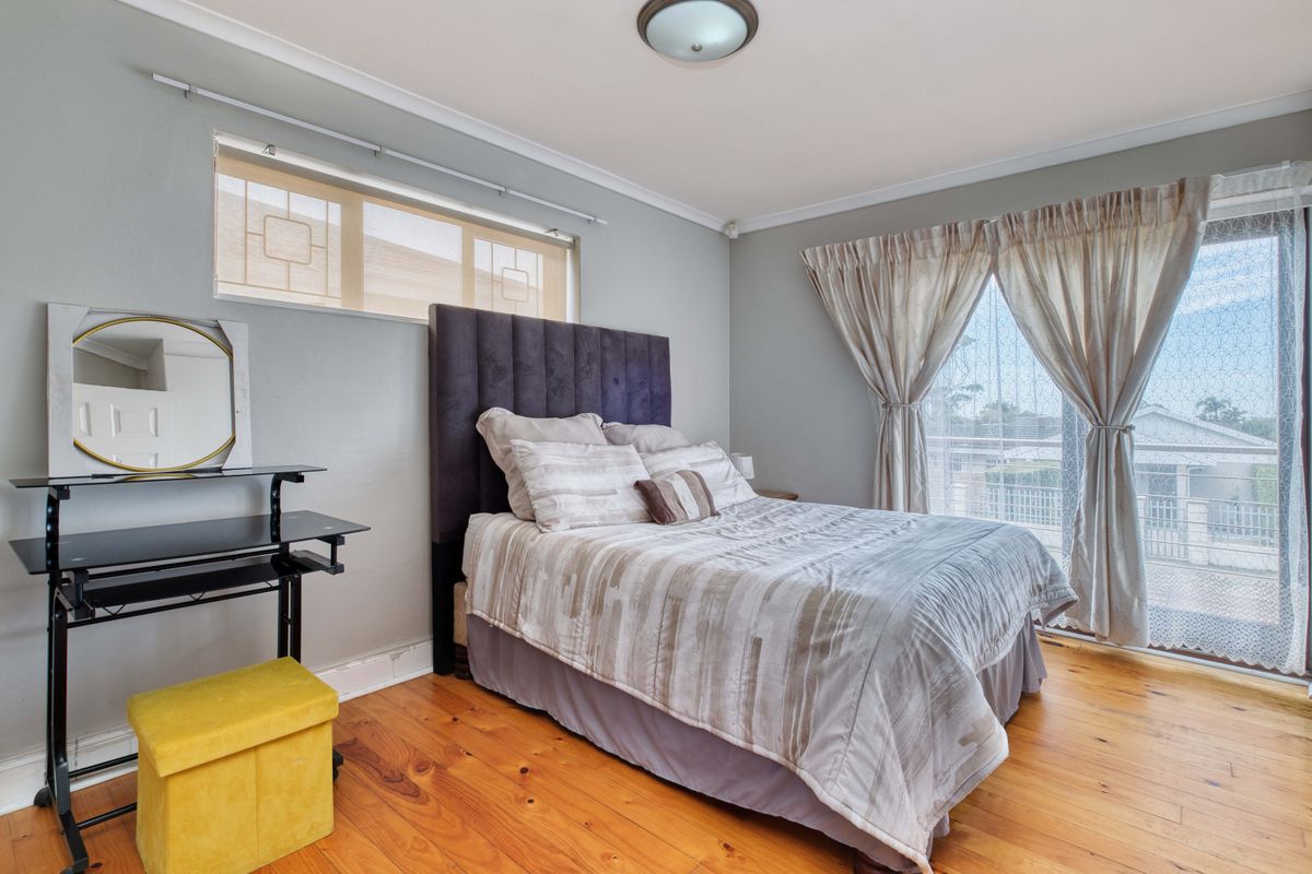 A well-lit bedroom featuring polished hardwood flooring, a sliding glass door leading to a balcony, and a high-level clerestory window.
