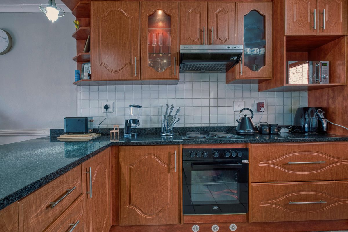 A functional kitchen featuring warm-toned laminate cabinetry, granite countertops, a tiled backsplash, and integrated appliances including an oven, hob, and extractor fan.