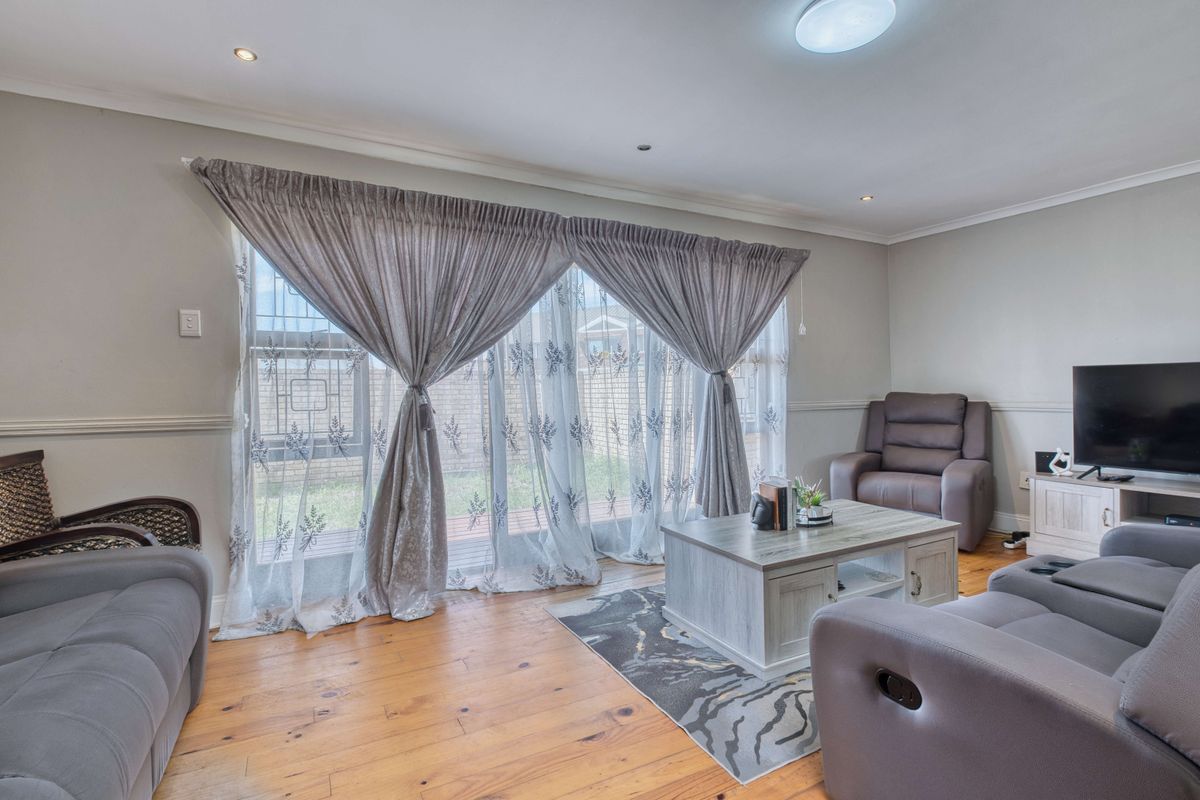 A comfortable living room featuring warm timber flooring, a chair rail, and large sliding glass doors that provide natural light and access to the exterior.