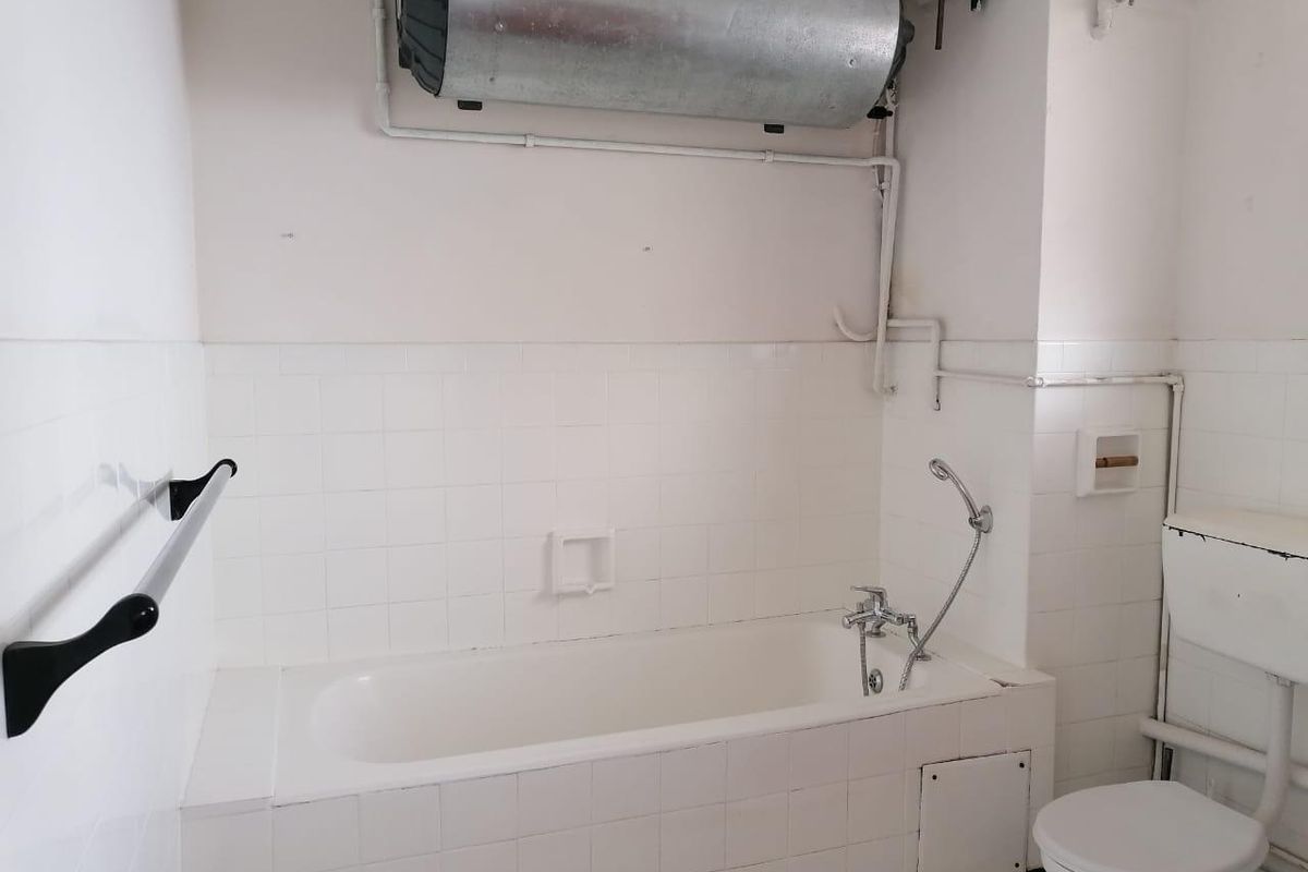 A functional bathroom featuring a standard bathtub, toilet, and wall-mounted electric water heater with exposed plumbing.