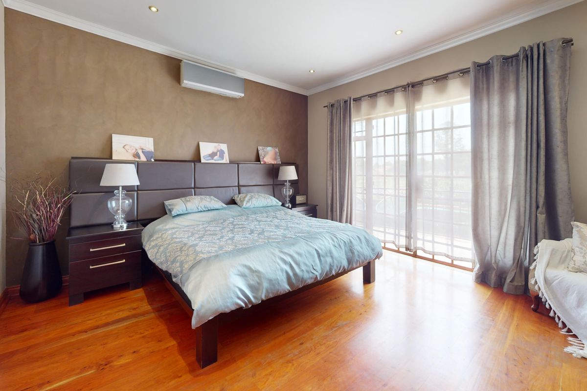 Spacious bedroom featuring warm hardwood flooring, recessed lighting, an integrated air conditioning unit, and large sliding glass doors providing natural light and outdoor access.