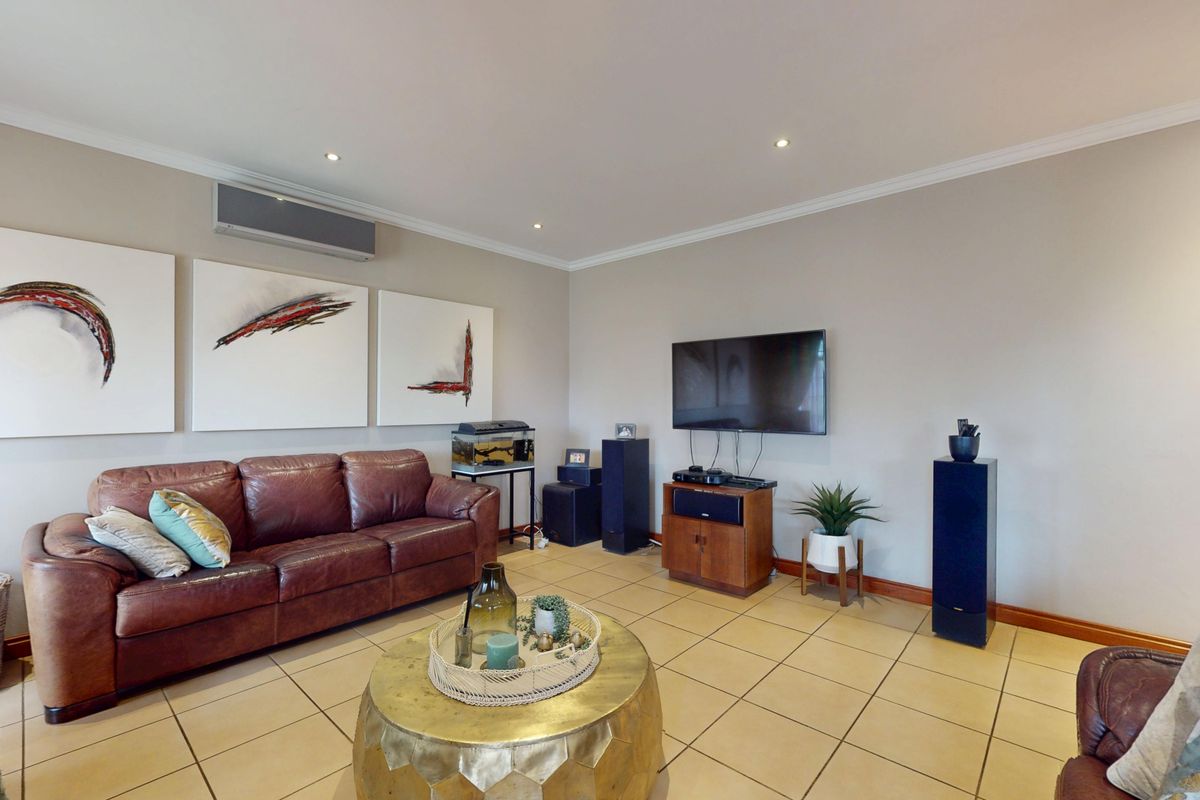 A comfortable living room featuring tiled flooring, recessed downlighting, and a wall-mounted air conditioning unit, providing a functional and well-maintained space.