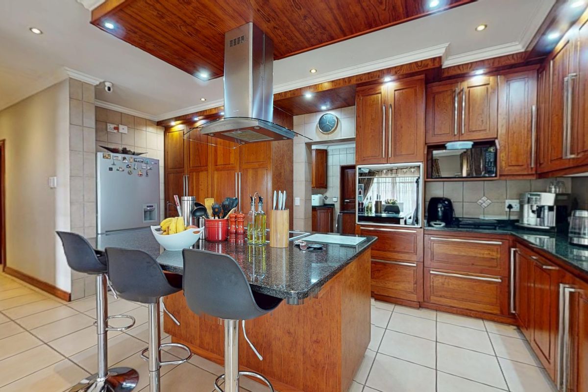 A well-appointed kitchen featuring rich wooden cabinetry, granite countertops, a central island, and integrated appliances, complemented by tiled flooring and recessed lighting.