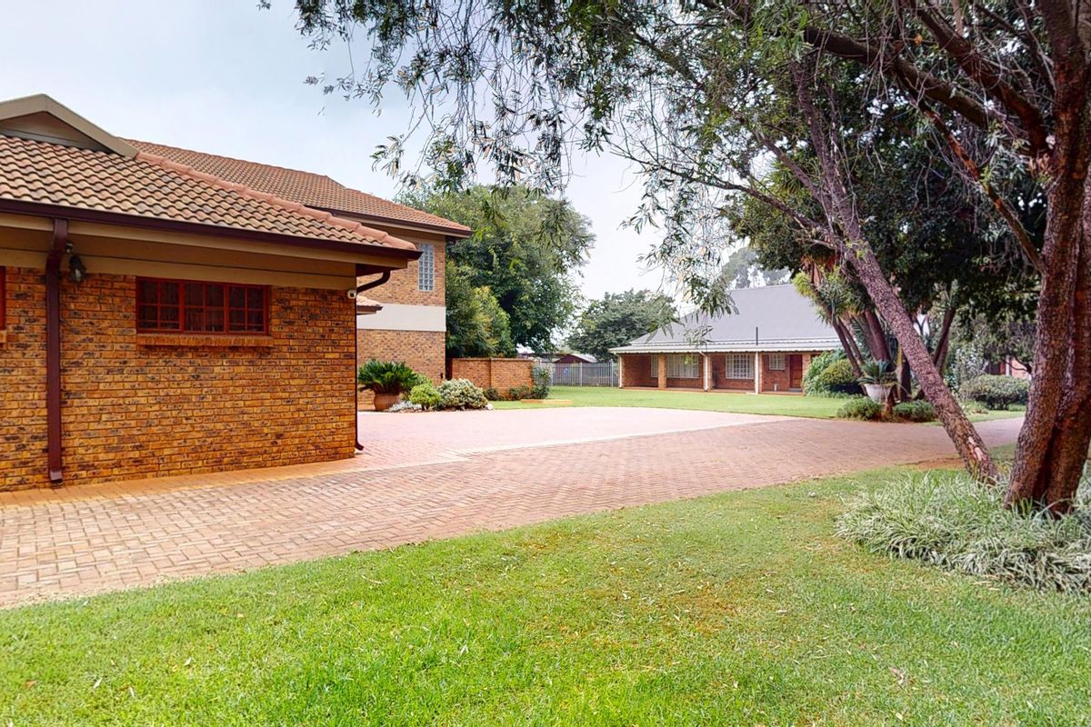 Spacious rear exterior view of the small holding featuring a well-maintained facebrick building, expansive paved driveway, and established garden surroundings.
