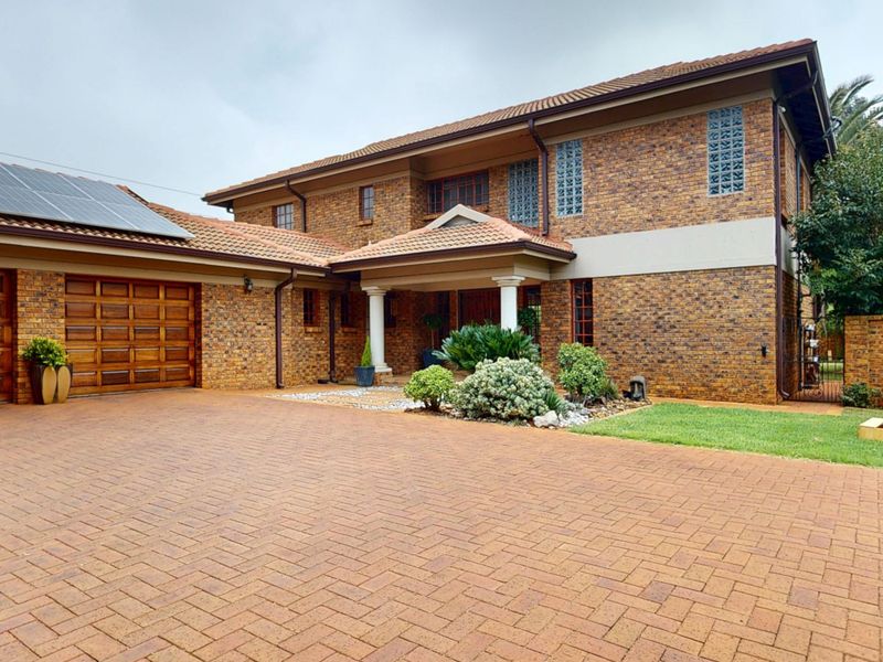 A well-maintained double-storey facebrick home featuring a paved driveway, double garage, covered entrance, and integrated solar panels on the roof.