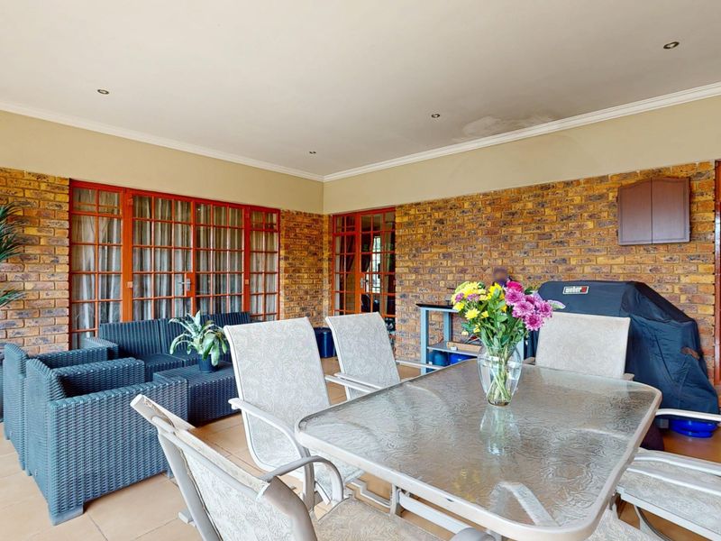 A covered patio area featuring exposed brick walls, tiled flooring, and multiple timber-framed glass doors providing access to the interior living spaces.