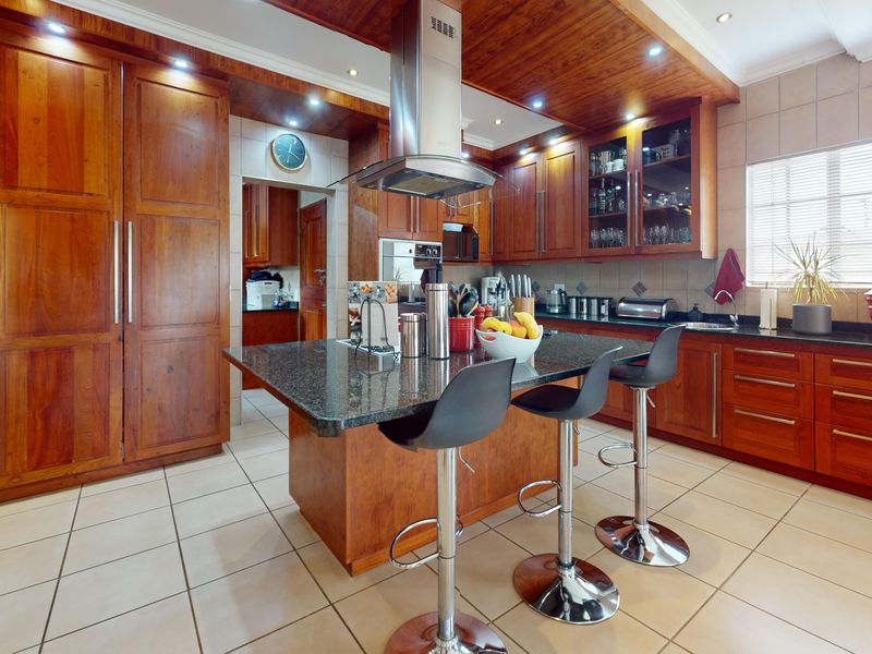 Spacious kitchen featuring warm wooden cabinetry, granite countertops, a central island with breakfast bar seating, and integrated stainless steel appliances.