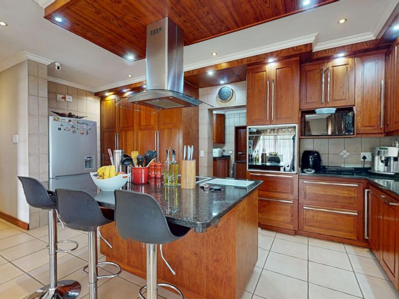 A well-appointed kitchen featuring rich wooden cabinetry, granite countertops, a central island, and integrated appliances, complemented by tiled flooring and recessed lighting.