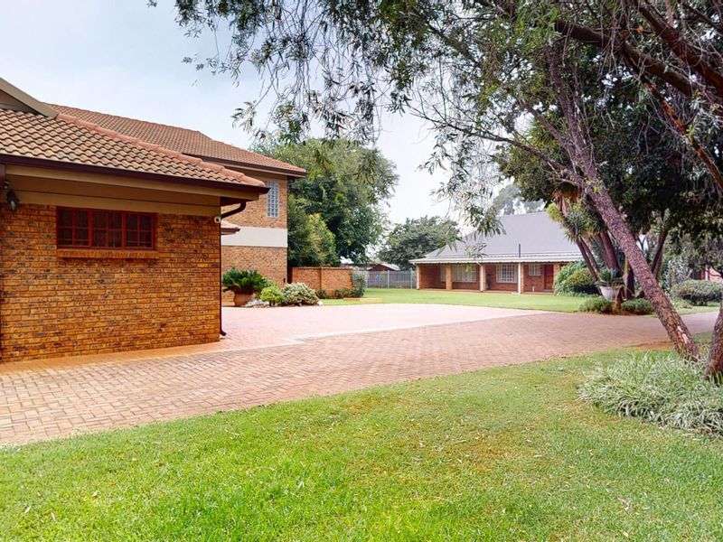 Spacious rear exterior view of the small holding featuring a well-maintained facebrick building, expansive paved driveway, and established garden surroundings.
