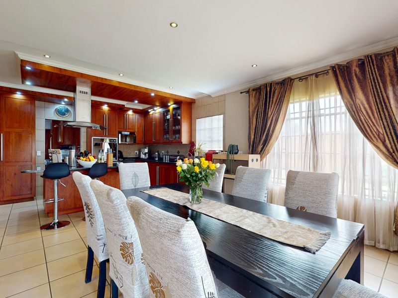 Open-plan kitchen and dining area featuring warm wooden cabinetry, a breakfast counter, recessed lighting, and tiled flooring throughout.