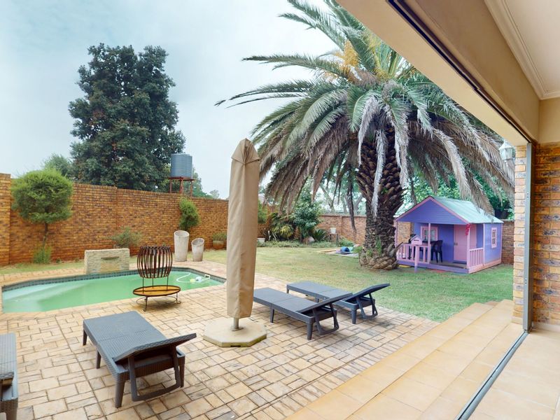 Outdoor entertainment area featuring a swimming pool, paved patio, and a large garden with established palm tree and brick boundary wall.