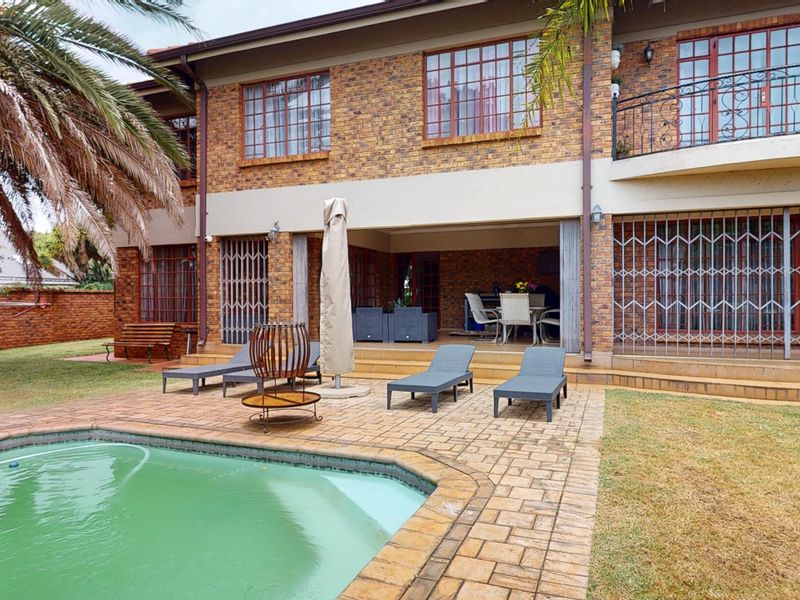 Rear view of a double-story brick home featuring a swimming pool, paved patio area, and an upper-level balcony with security gates.