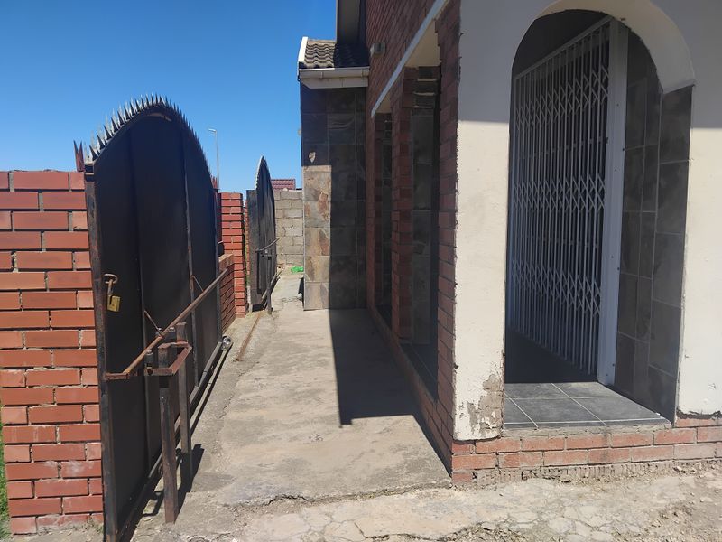 Front entrance area featuring a brick facade, security gate, and a concrete pathway leading to the main door.