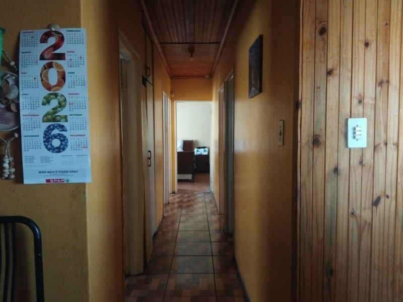 A narrow residential hallway featuring tiled flooring and a timber-paneled ceiling, providing access to multiple rooms within the home.