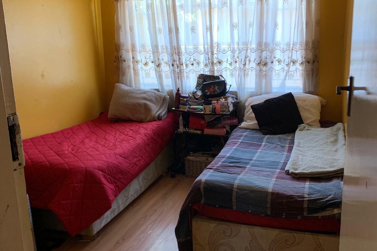 A compact bedroom featuring laminate flooring and a window with a curtain rod, currently utilized as a twin room.