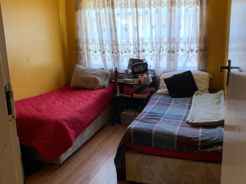 A compact bedroom featuring laminate flooring and a window with a curtain rod, currently utilized as a twin room.