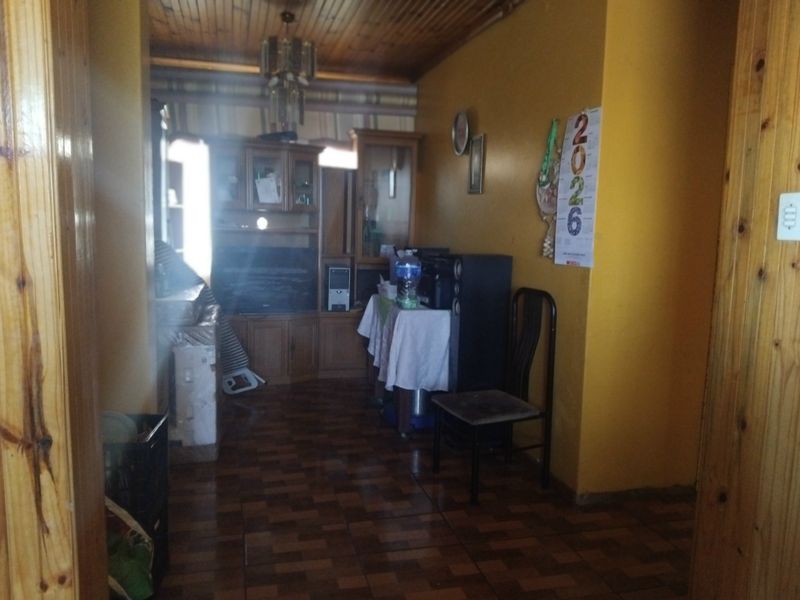 A living room featuring timber ceiling paneling and tiled flooring, offering a dated aesthetic with built-in cabinetry.