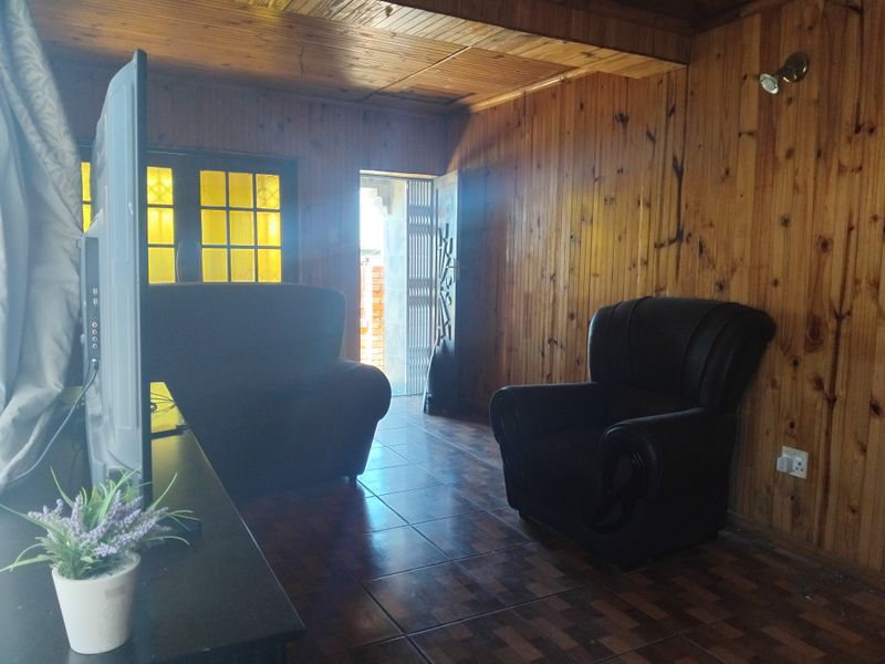 Living room featuring extensive timber wall paneling, a timber ceiling, and tiled flooring, with access to an exterior area through a security gate.