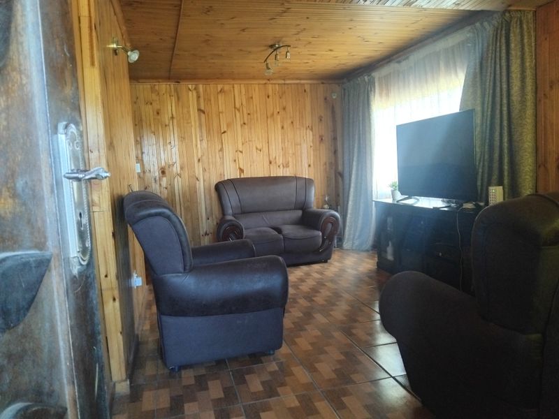 A living room featuring extensive timber wall and ceiling paneling with tiled flooring, offering a rustic aesthetic.