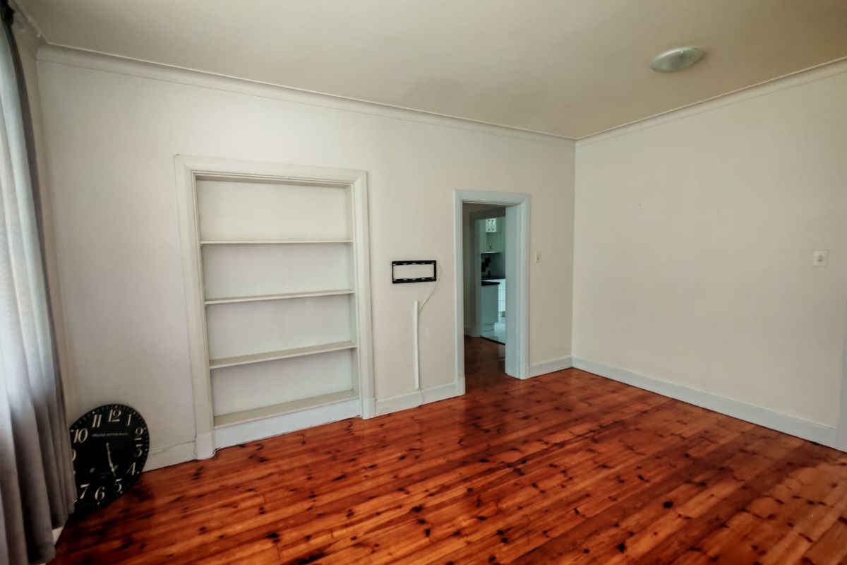 A bright living room featuring polished timber flooring, built-in shelving, and a doorway leading to the kitchen area.