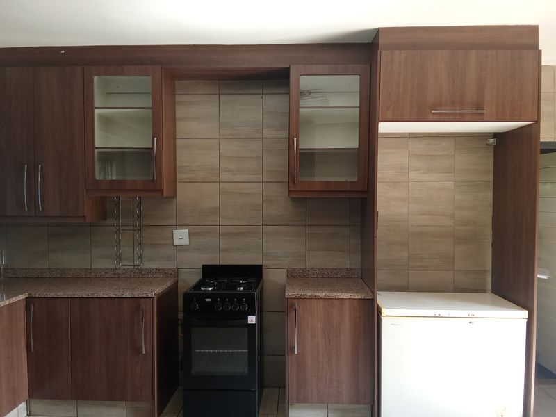 A functional kitchen featuring wood-finish cabinetry, granite countertops, tiled backsplash, and a dedicated space for a refrigerator.