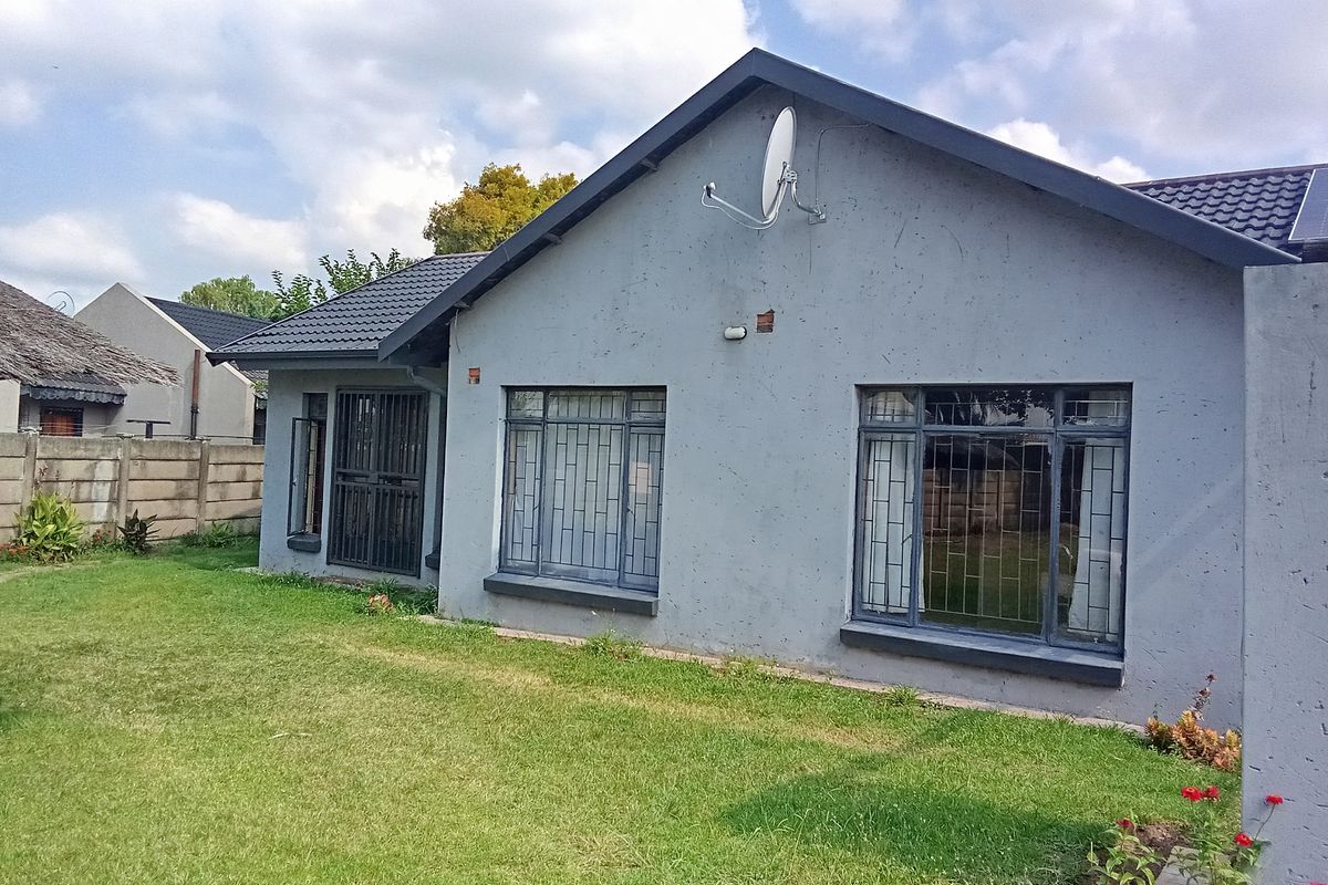 Rear view of a single-story house featuring a tiled roof, grey exterior walls, security bars on windows, and a private lawn area.