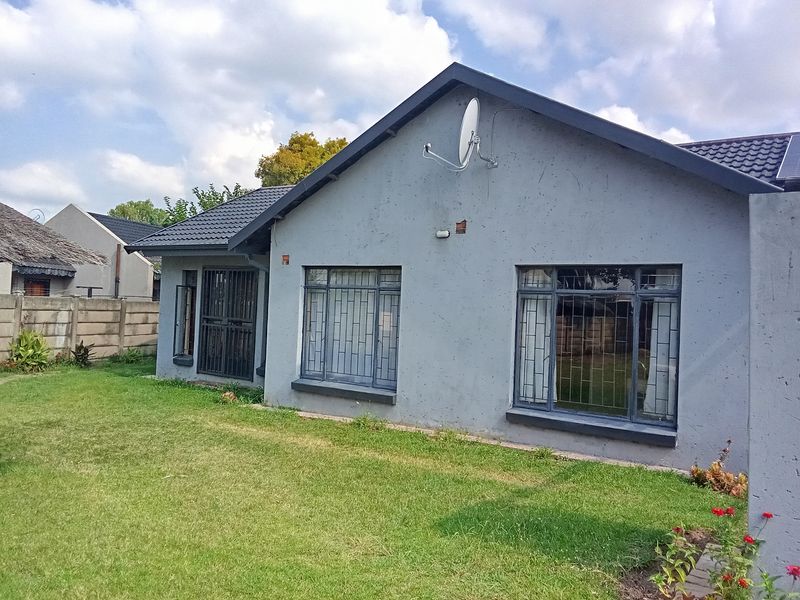 Rear view of a single-story house featuring a tiled roof, grey exterior walls, security bars on windows, and a private lawn area.