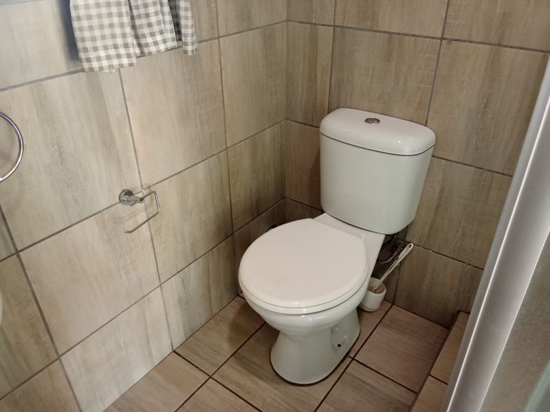 A compact bathroom featuring neutral wood-look floor and wall tiles, equipped with a standard white toilet and chrome fixtures.