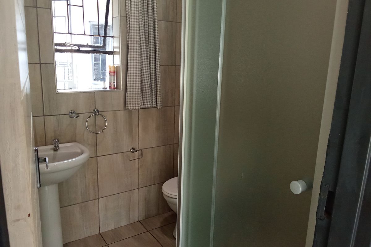 A compact bathroom featuring a pedestal basin, toilet, and shower enclosure with neutral ceramic wall and floor tiling.