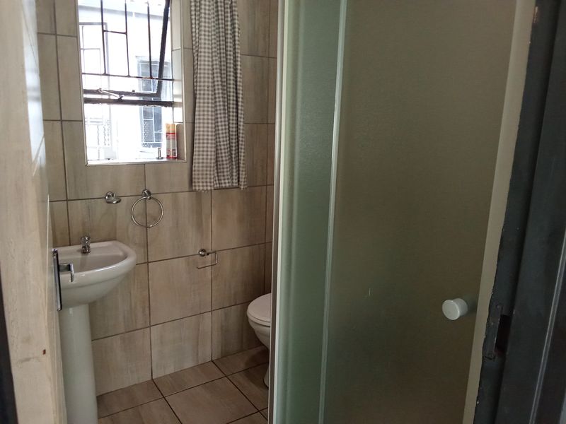 A compact bathroom featuring a pedestal basin, toilet, and shower enclosure with neutral ceramic wall and floor tiling.