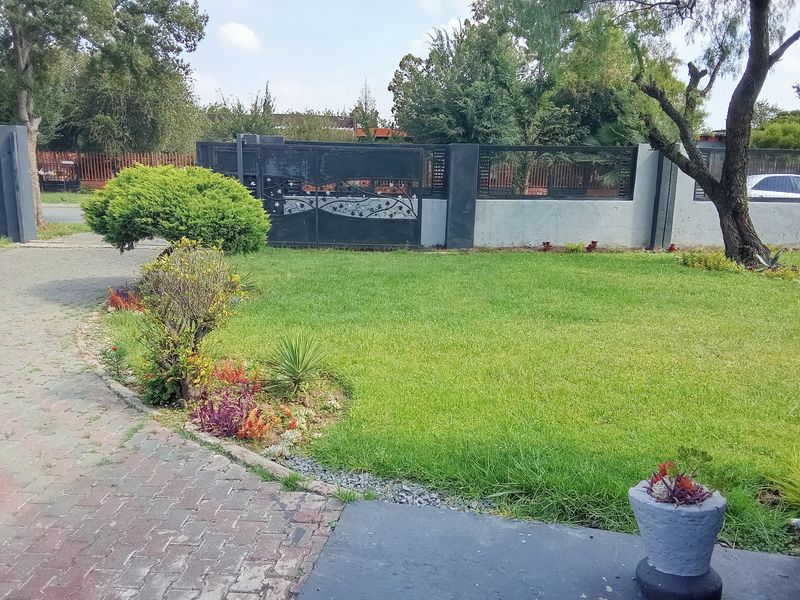 Front garden area featuring a paved driveway, manicured lawn, and a secure metal gate with perimeter walling.
