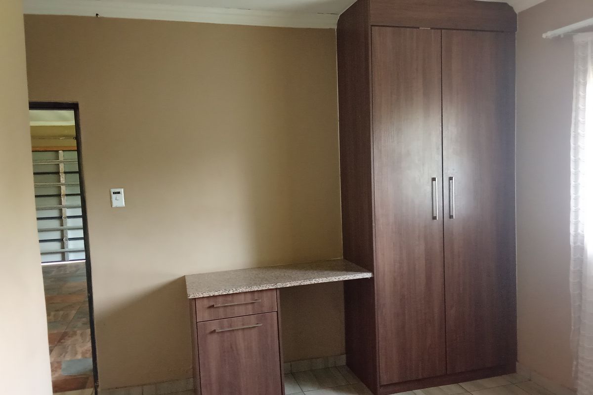A bedroom featuring a built-in wardrobe and integrated desk with a granite countertop, finished with tiled flooring.