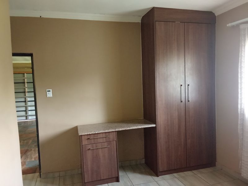 A bedroom featuring a built-in wardrobe and integrated desk with a granite countertop, finished with tiled flooring.