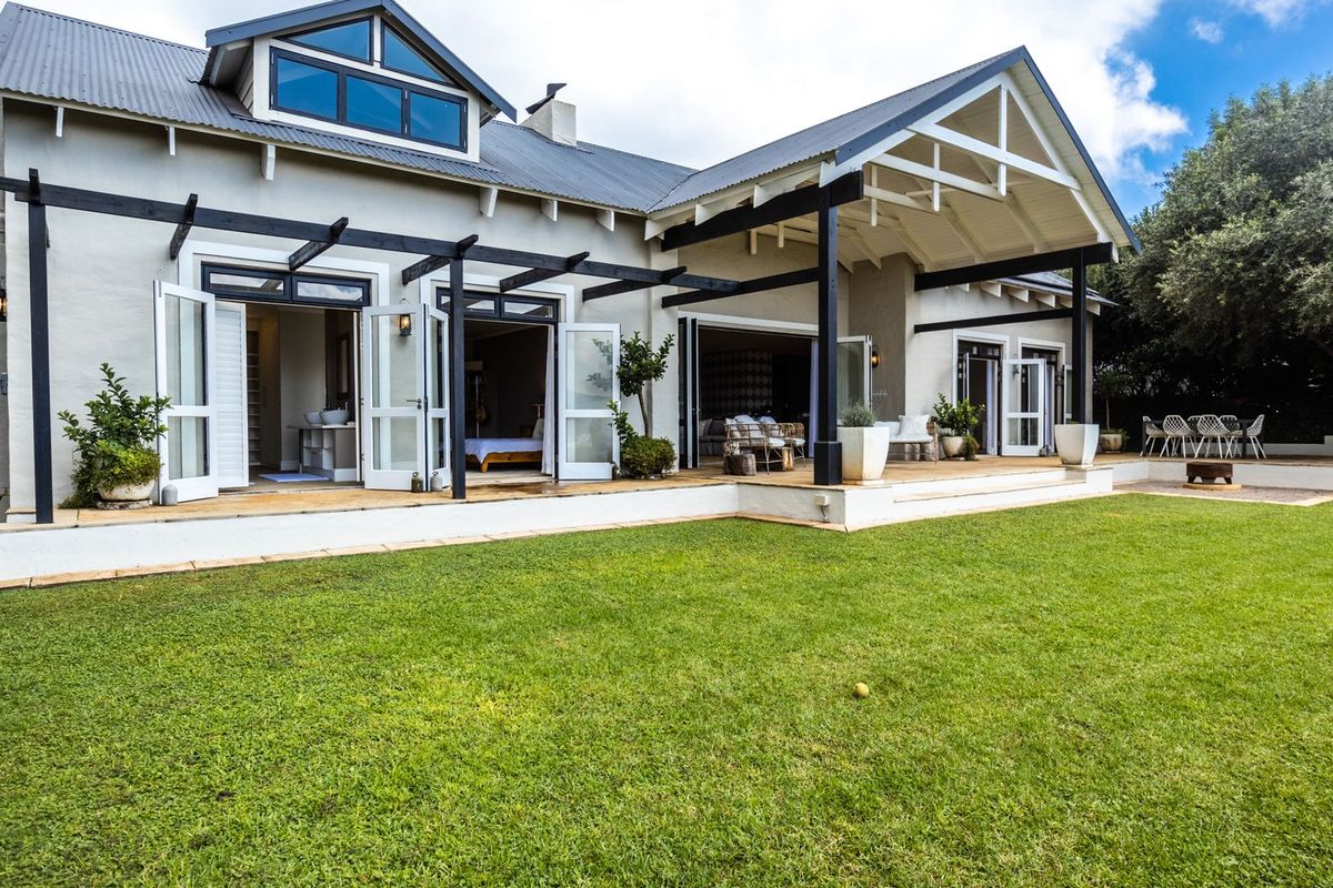 Spacious rear exterior featuring a large lawn, timber decking, and a covered patio area with multiple sets of french doors leading into the home.