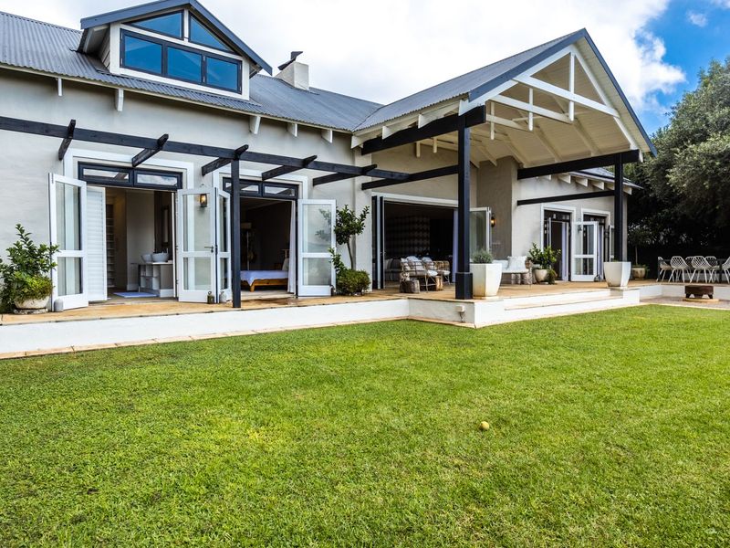 Spacious rear exterior featuring a large lawn, timber decking, and a covered patio area with multiple sets of french doors leading into the home.