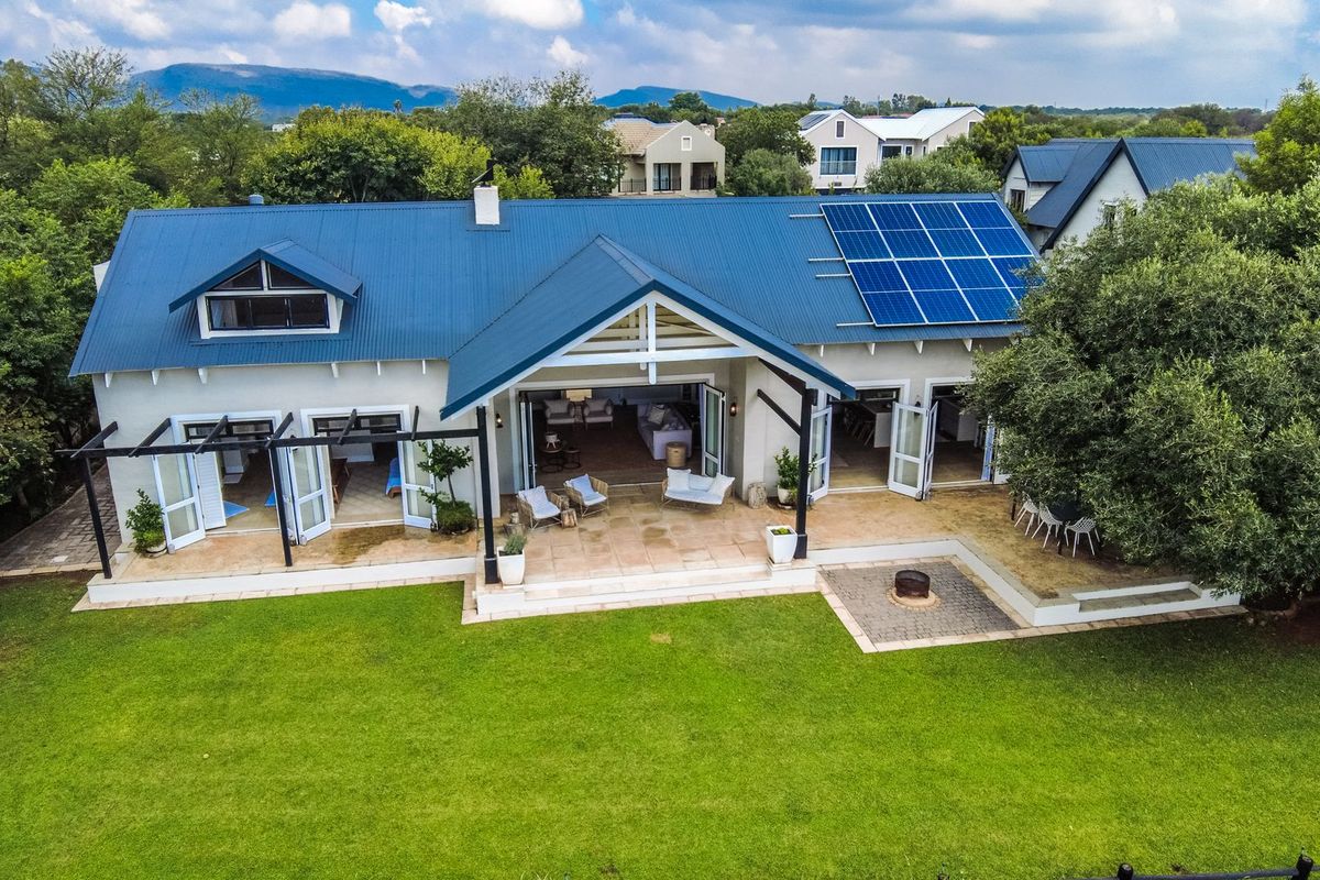 Aerial view of a well-maintained residence featuring a metal roof with integrated solar panels, a spacious covered patio, and a landscaped rear garden.