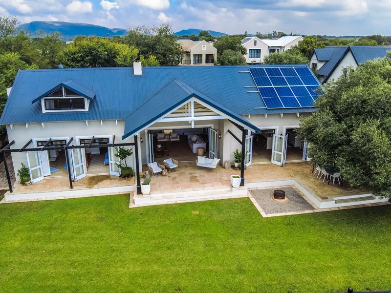 Aerial view of a well-maintained residence featuring a metal roof with integrated solar panels, a spacious covered patio, and a landscaped rear garden.