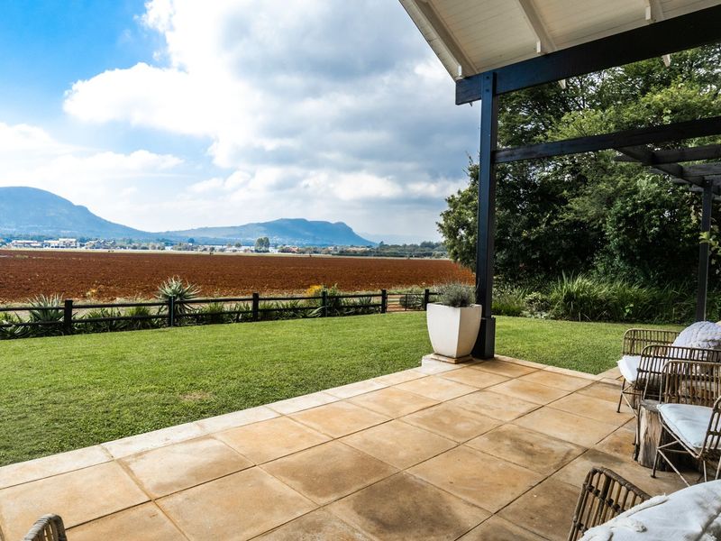 A spacious covered patio featuring paved flooring and a timber pergola, offering expansive views over the garden and surrounding landscape.