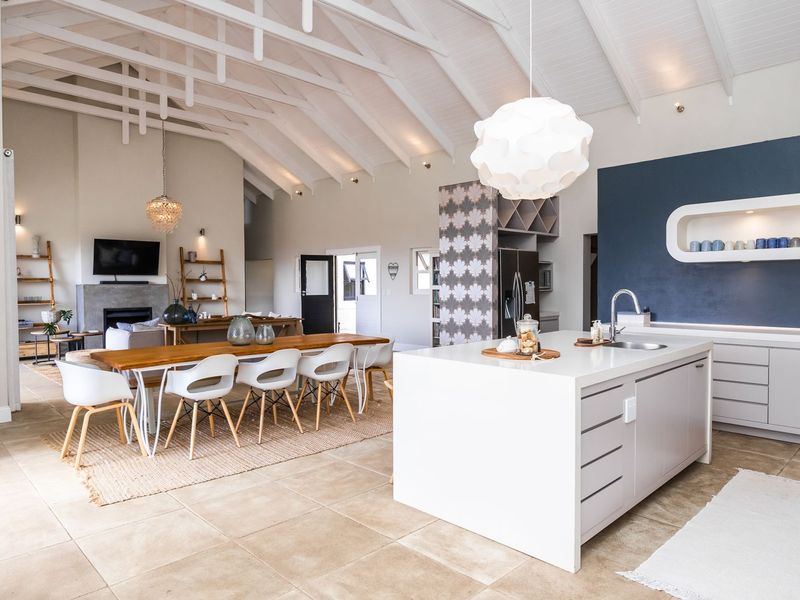 Spacious open-plan living area featuring a modern kitchen island, vaulted ceilings with exposed rafters, and a cozy fireplace, finished with neutral tiled flooring.