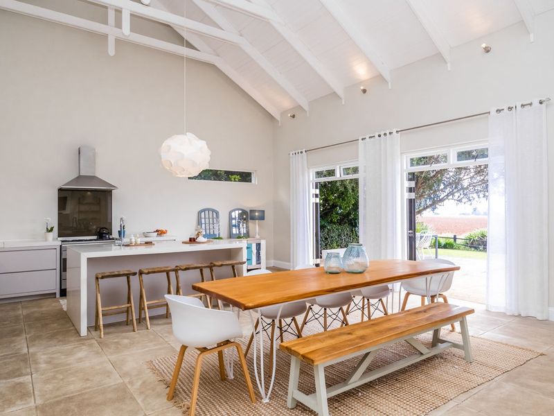 Spacious open-plan kitchen and dining area featuring vaulted ceilings, exposed rafters, a central island, and large sliding doors opening to the garden.