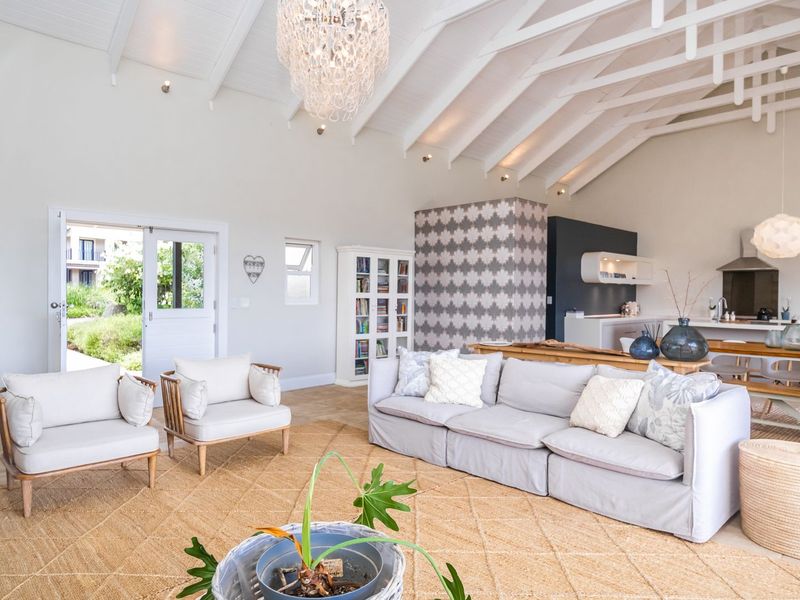 Spacious open-plan living and kitchen area featuring high vaulted ceilings with exposed beams, tiled floors, and direct access to the garden through french doors.